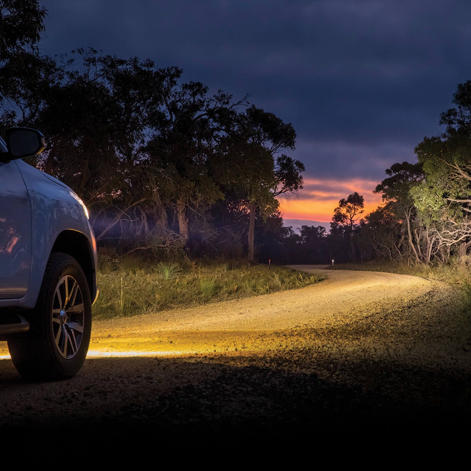 A car shines bright white light onto a country road from its headlights